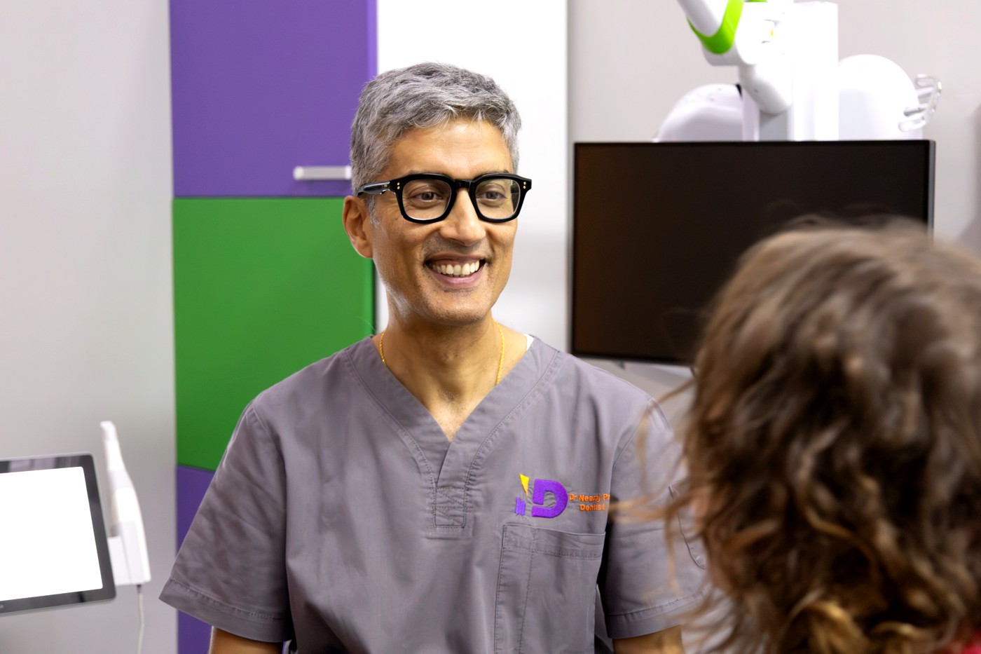 Dr Neeraj Puri in grey scrubs smiling and talking with a patient at Integrated Dentalcare, Edinburgh