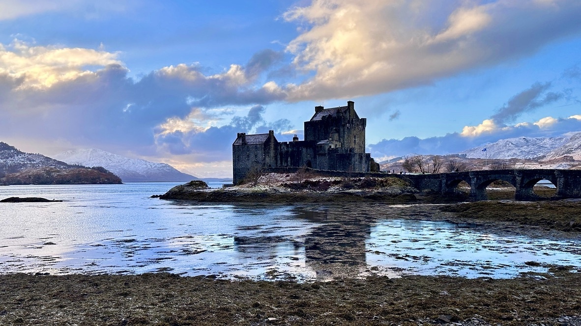 Eilean Donan Castle near Skye in the Scottish Highlands, with snow-capped mountains and its stone bridge reflected in the loch