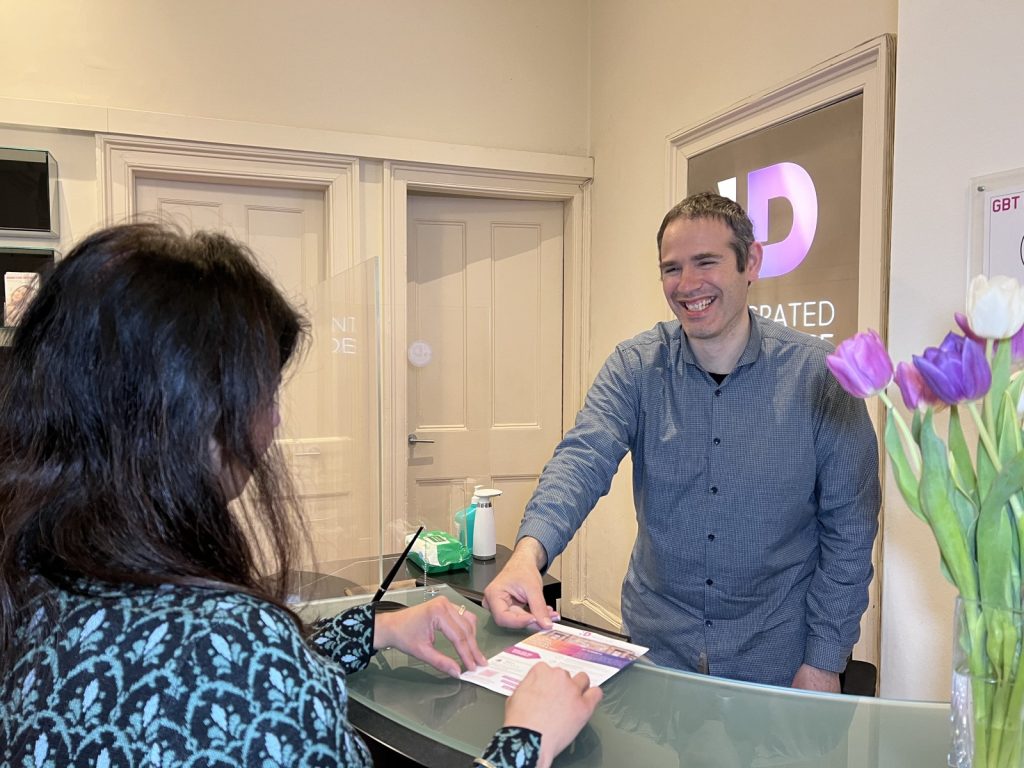 Nuno welcoming a visitor at reception and handing over an information leaflet, Integrated Dentalcare, Edinburgh